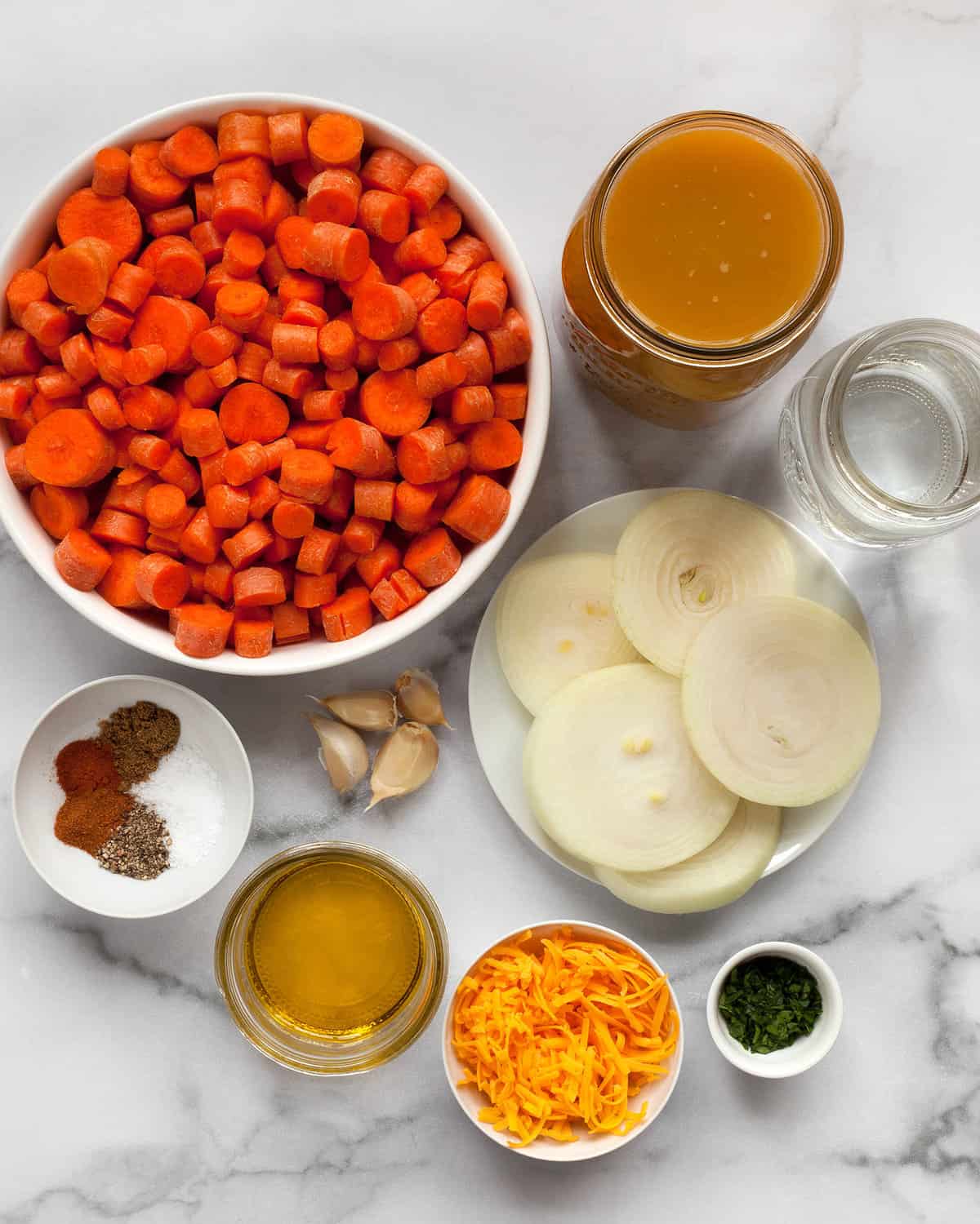 Ingredients for soup including carrots, onions, garlic, spices, vegetable broth, cheddar and parsley.