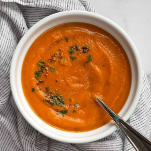 Bowl of carrot soup topped with parsley and black pepper.