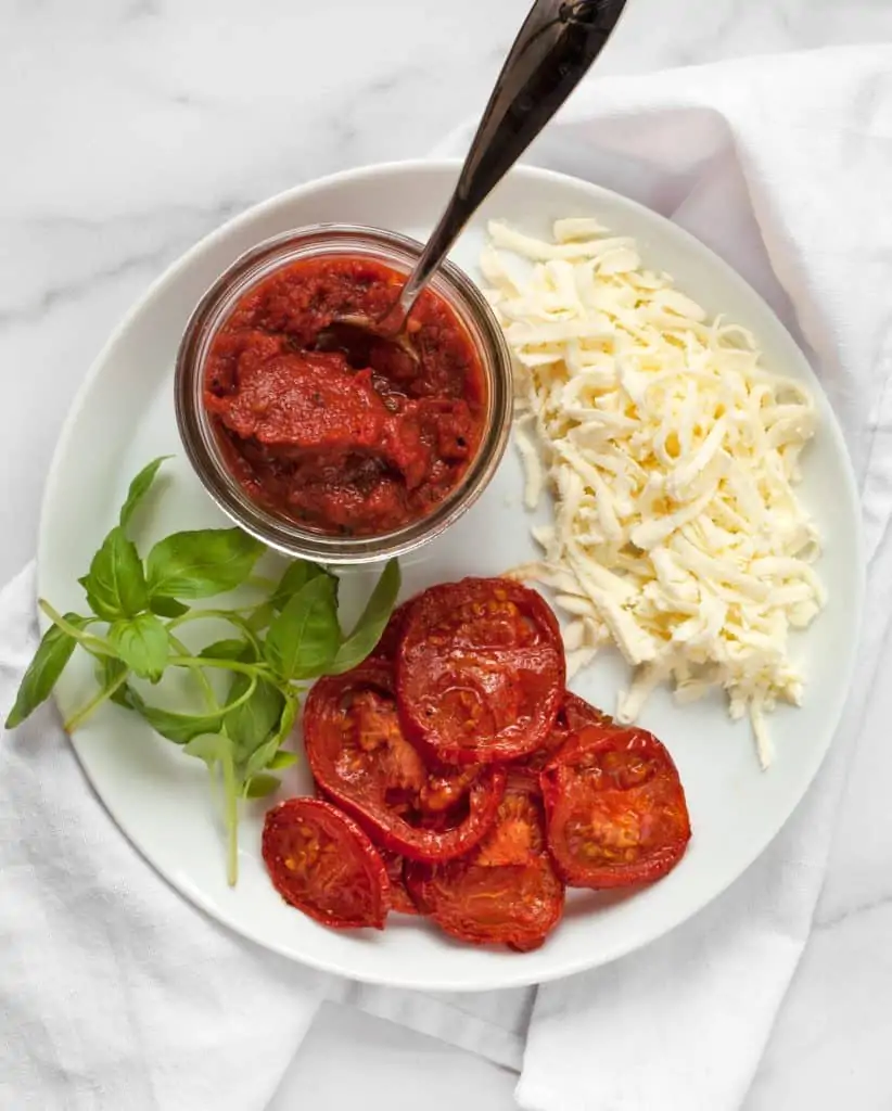 Tomato sauce, shredded cheese, roasted tomatoes and basil on a plate
