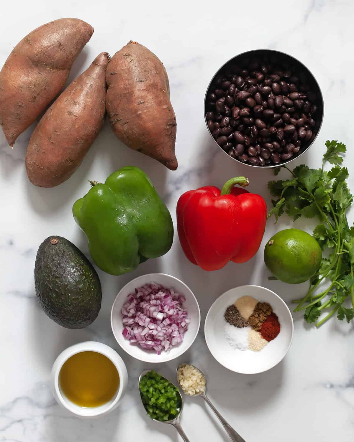 Salad ingredients including sweet potatoes, peppers, black beans, jalapenos, garlic, spices, avocado, red onions, cilantro and olive oil.