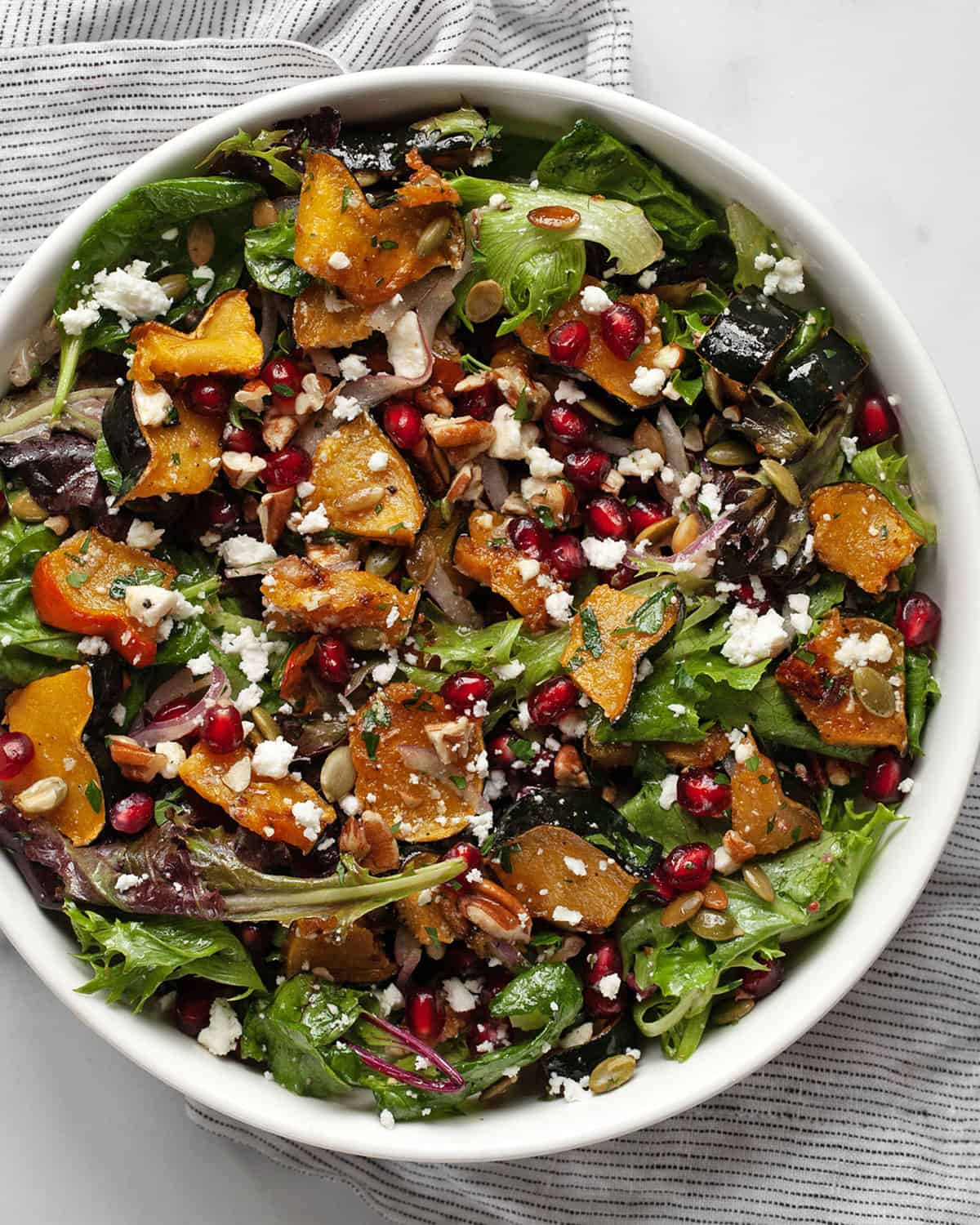 Fall slam with acorn squash, pomegranate seeds, pumpkin seeds, goat cheese and pecans in a bowl.