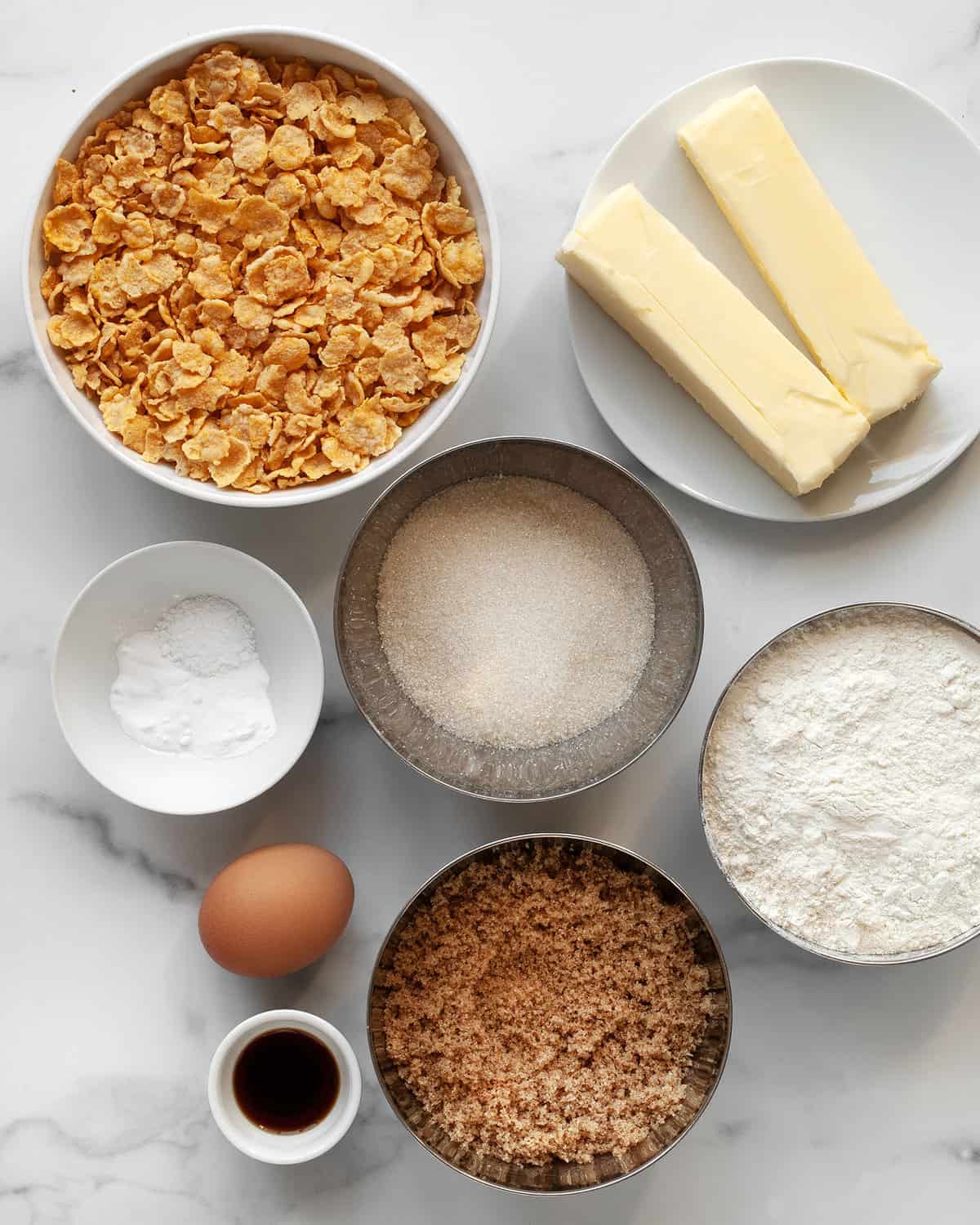 Ingredients for cookies including cornflakes, flour, egg, butter, vanilla extract, granulated sugar, light brown sugar and egg.