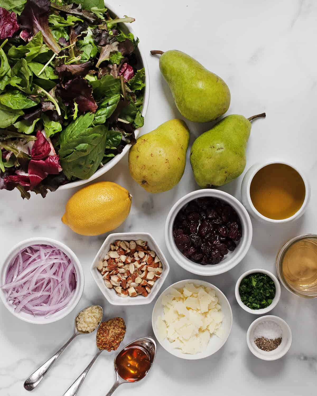 Ingredients including pears, mixed greens, lemon, almonds, manchego, red onions, parsley, oil, vinegar, salt and pepper.