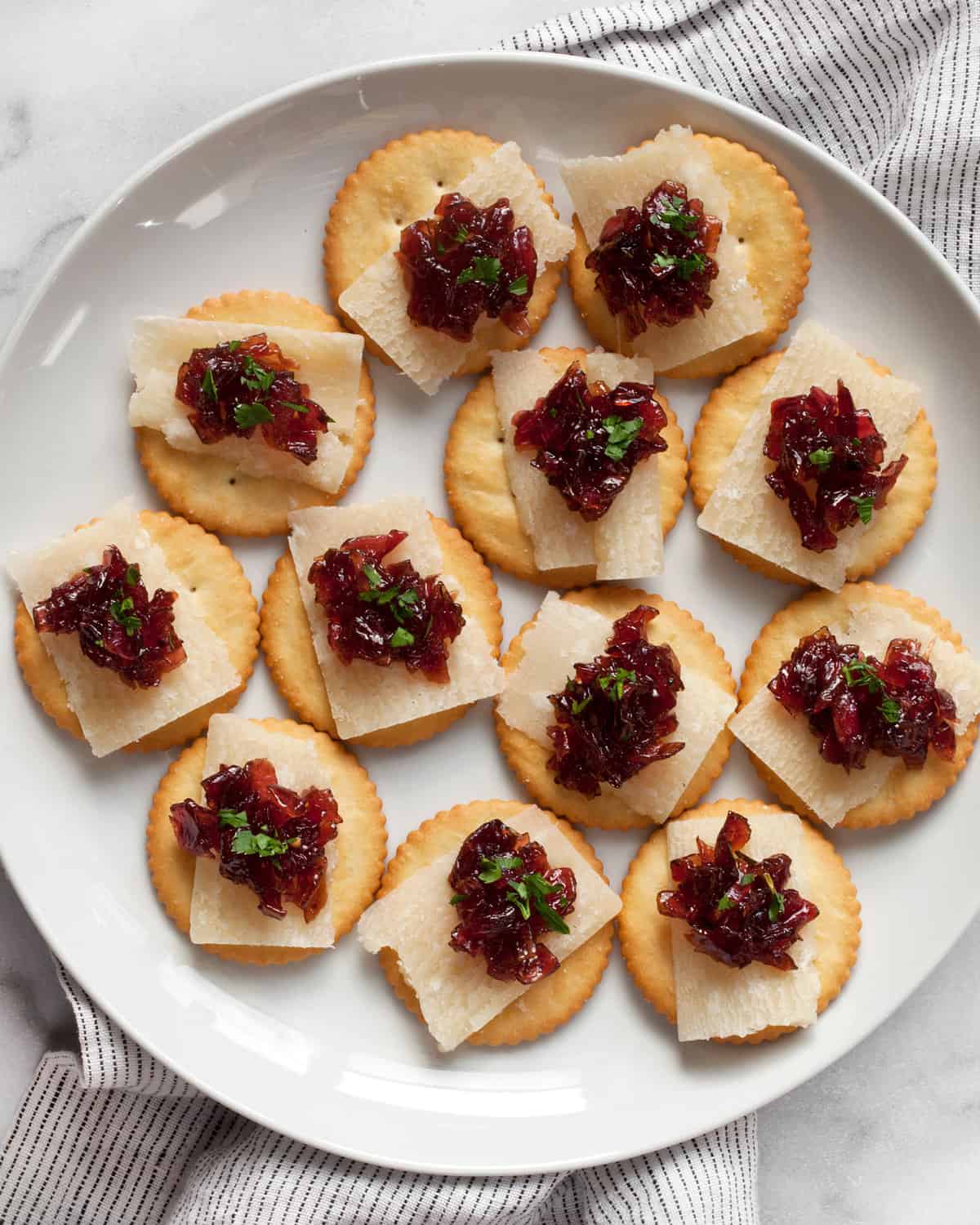 Plate of crackers topped with Parmesan slices and onion jam.