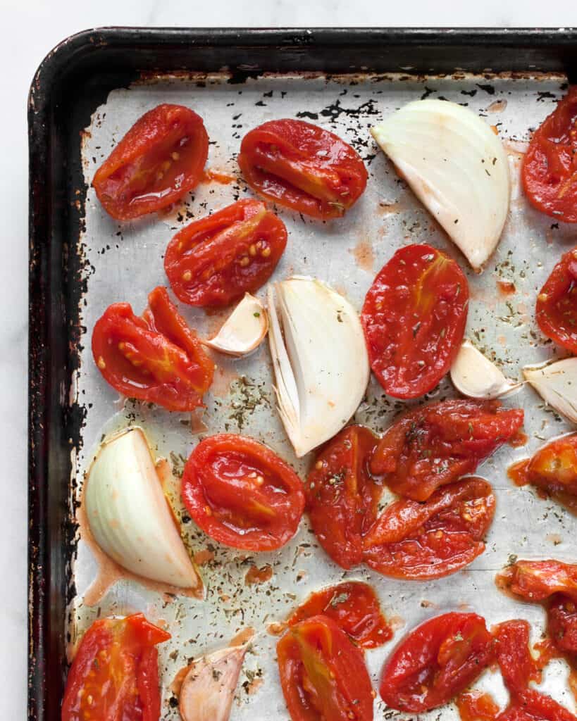 Halved canned tomatoes, onions and garlic on a sheet pan