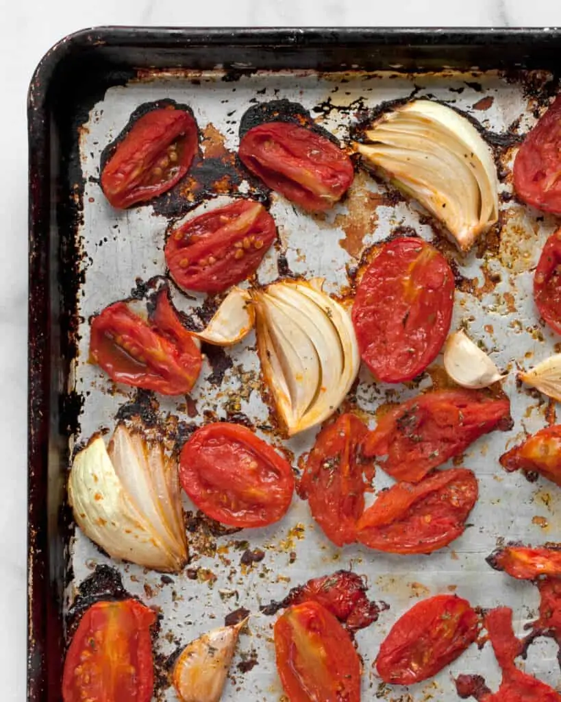 Roasted halved canned tomatoes, onions and garlic on a sheet pan