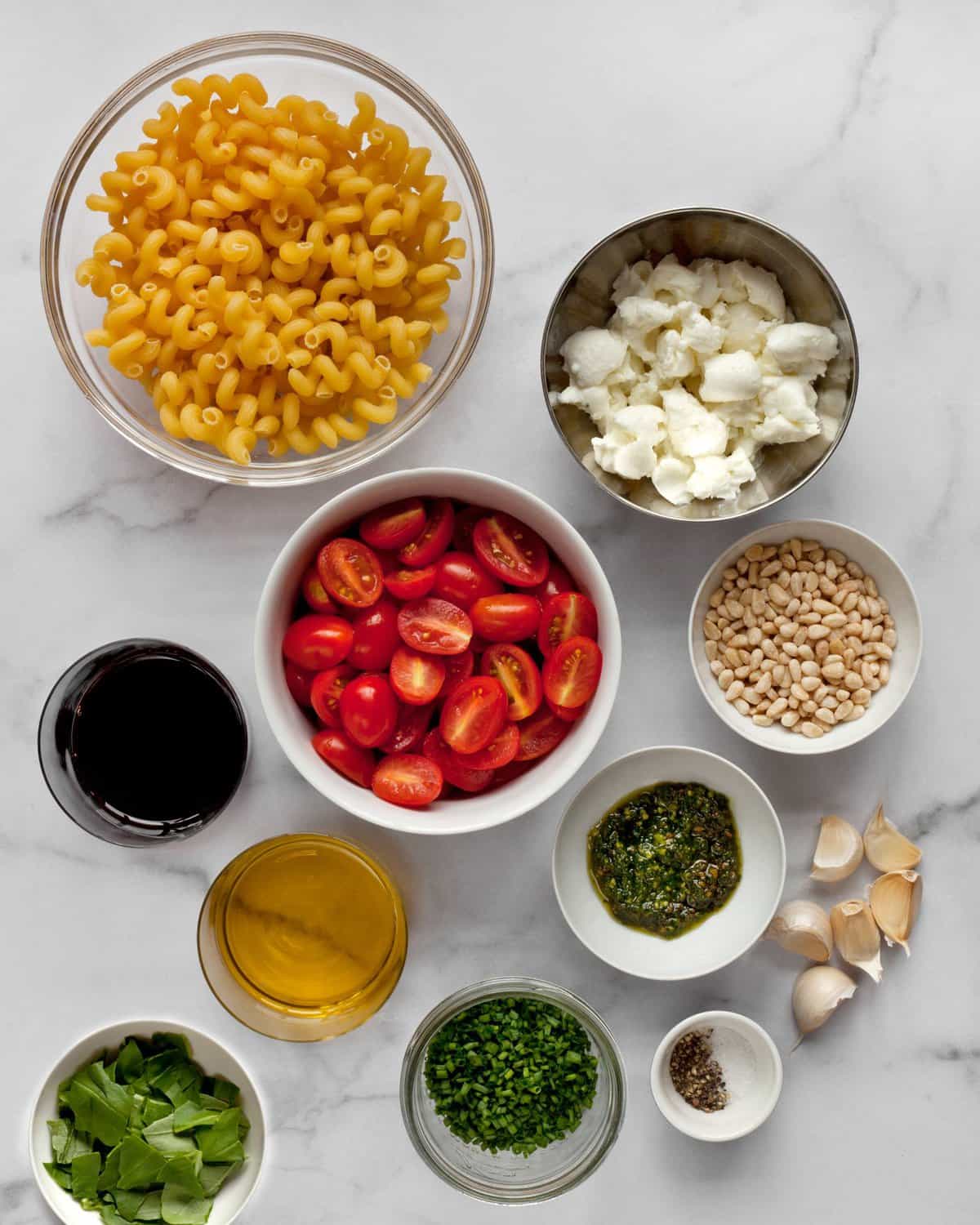 Ingredients including pasta, tomatoes, mozzarella, basil, pesto, olive oil and garlic.