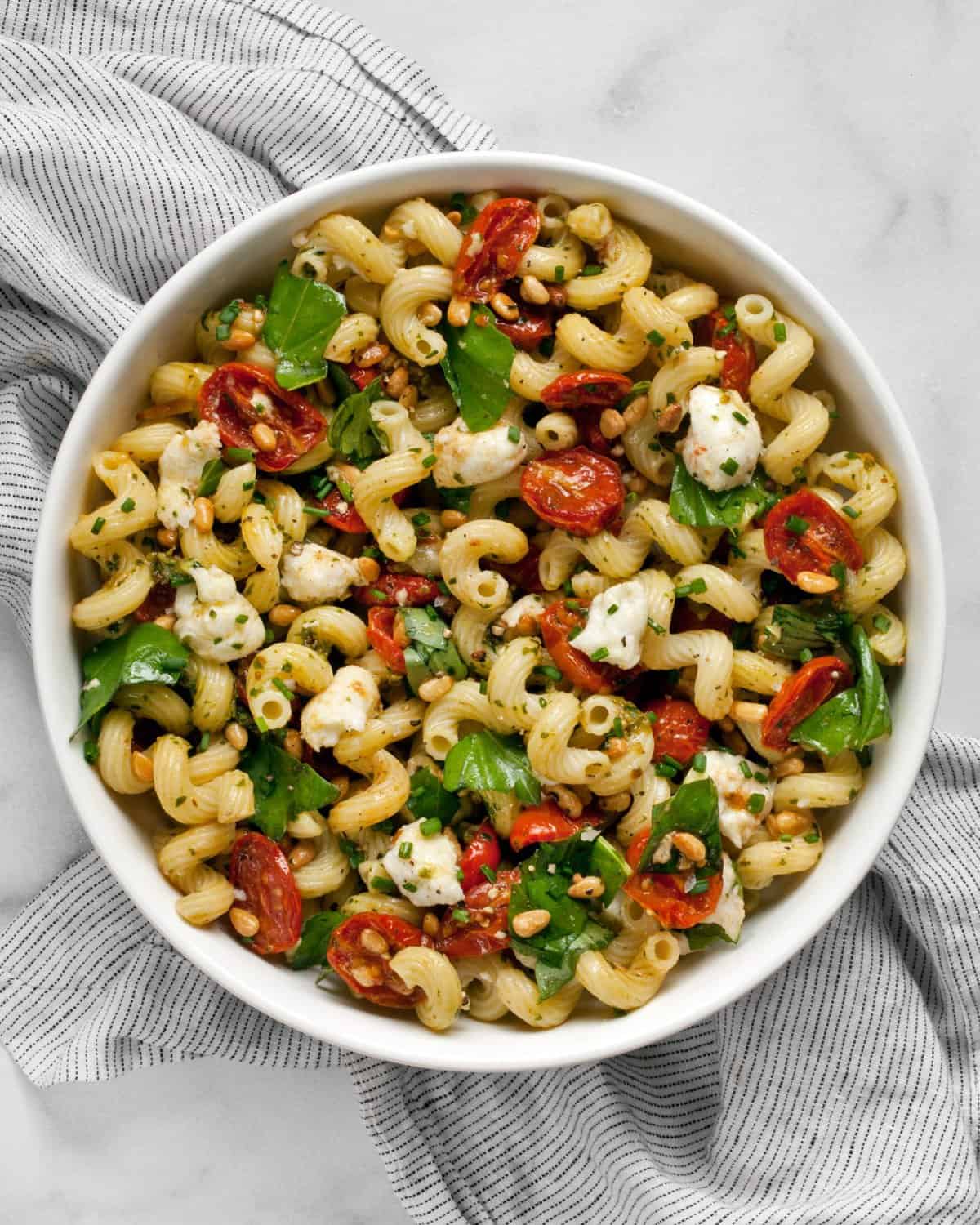 Pesto pasta salad with roasted tomatoes and mozzarella in a bowl.