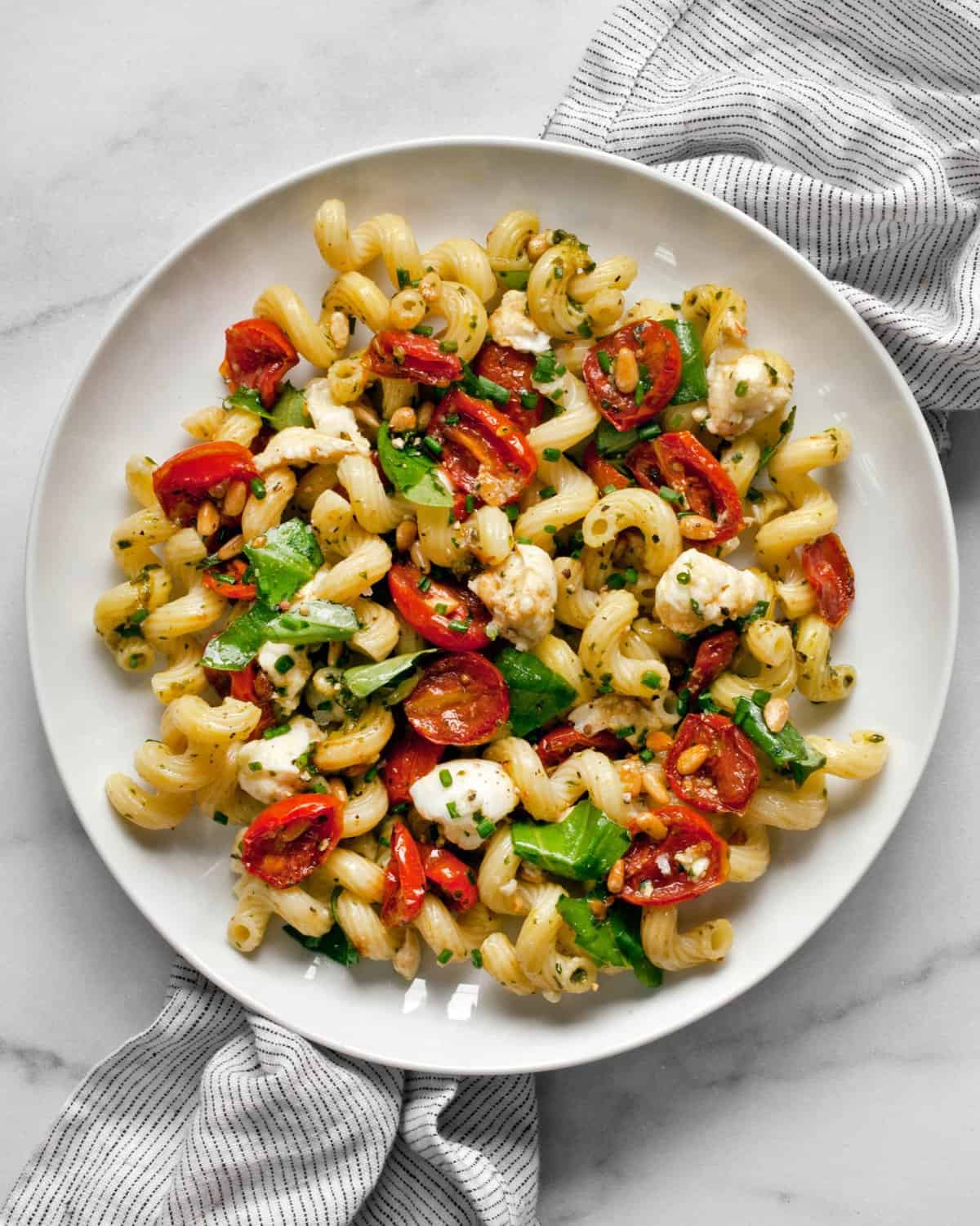 Pesto pasta salad with roasted tomatoes and mozzarella on a plate.