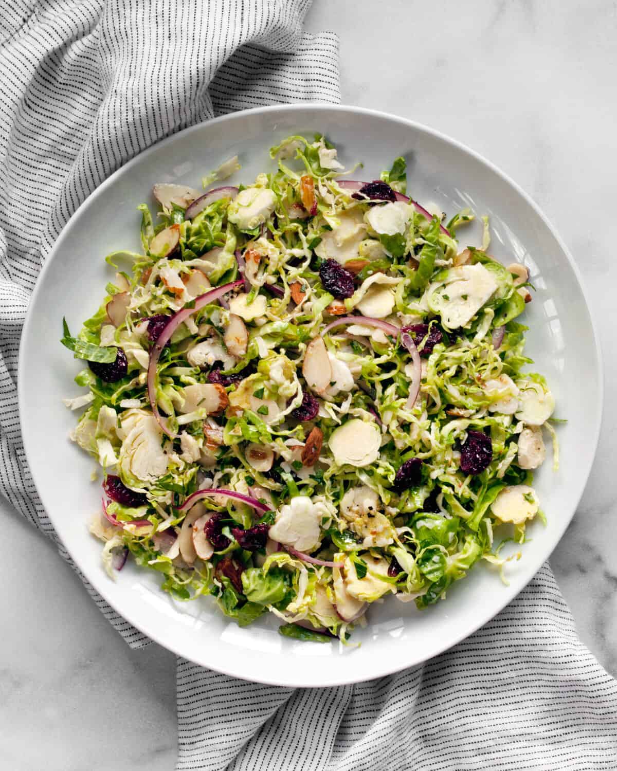 Salad with brussels sprouts, cranberries, parmesan, almonds and red onions on a plate.