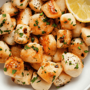 Seared bay scallops in a bowl with lemon slices.
