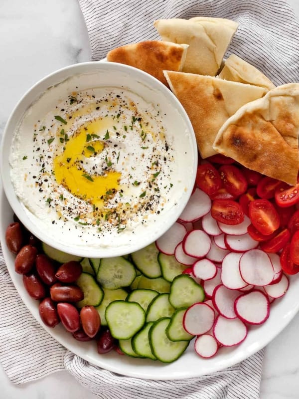 Labneh in a bowl with a platter of pita, tomatoes, radishes, cucumbers and olives