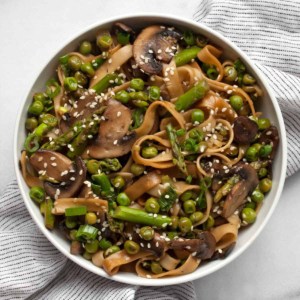 Udon noodle stir-fry with asparagus, mushrooms and peas in a bowl.