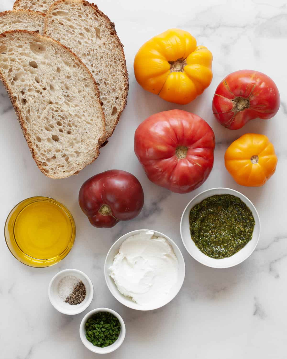 Ingredients including heirloom tomatoes, bread, olive oil, salt, pepper, pesto, cheese and chives.