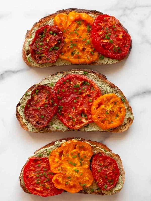 Three slices of toast topped with roasted tomatoes and pesto cheese spread.