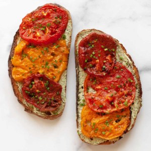 Two slices of toast with roasted tomatoes and pesto cheese spread.