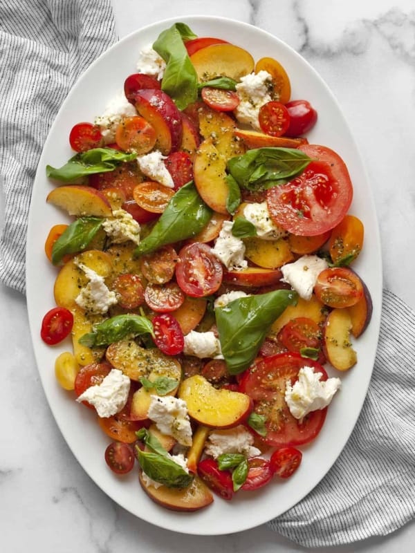 Caprese salad with peaches on an oval platter.