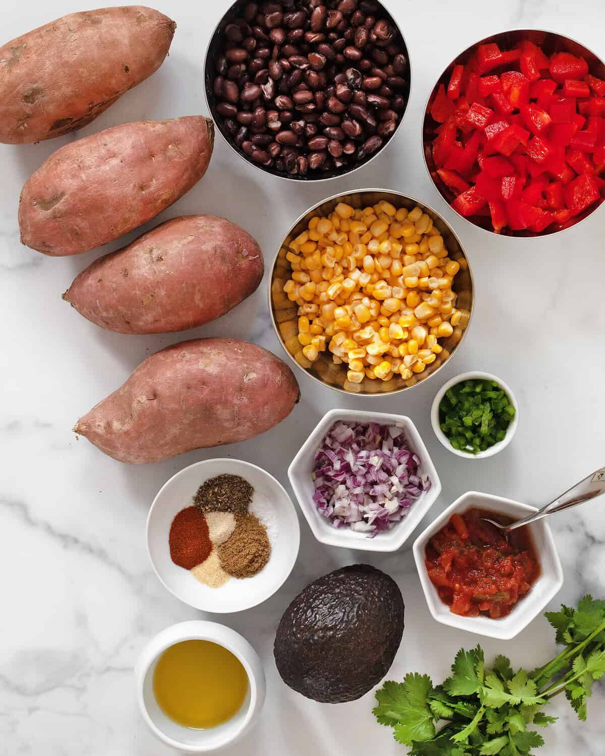 Ingredients including sweet potatoes, black beans, corn, red peppers, red onions, spices, salsa, avocado, cilantro, jalapenos and olive oil.