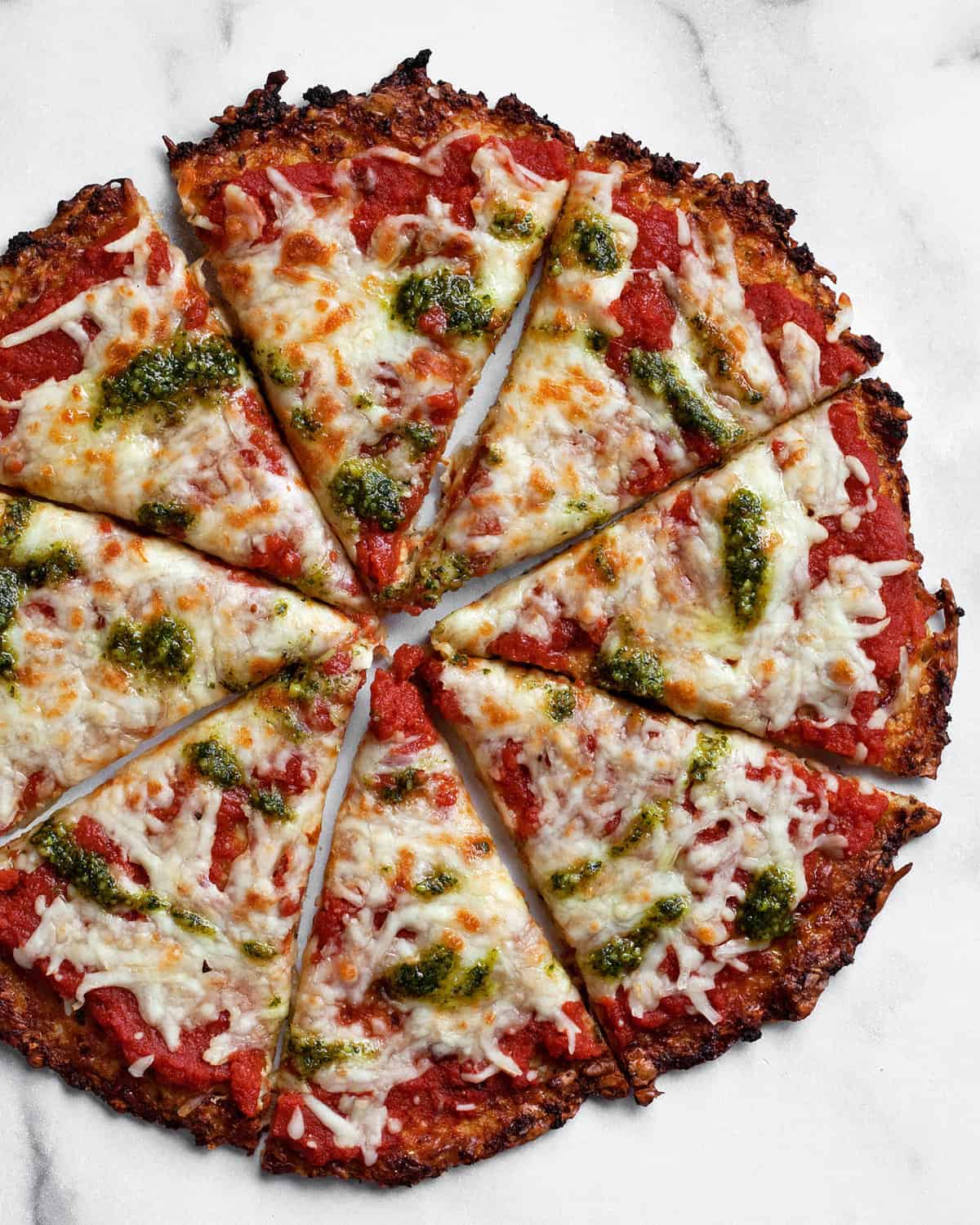 Cauliflower crust pizza drizzled with pesto and cut into slices.