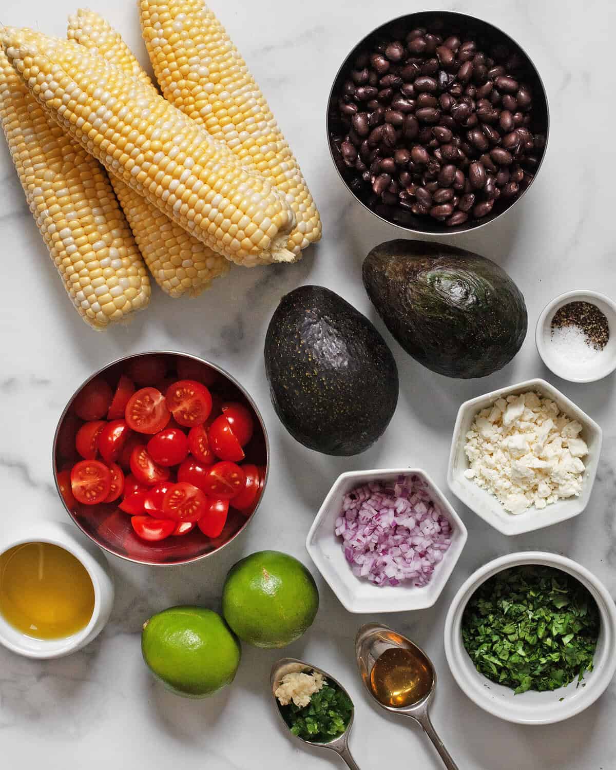 Ingredients including corn, black beans, avocados, tomatoes, limes, red onions, feta, cilantro, salt, pepper, jalapenos, garlic, oil and honey.