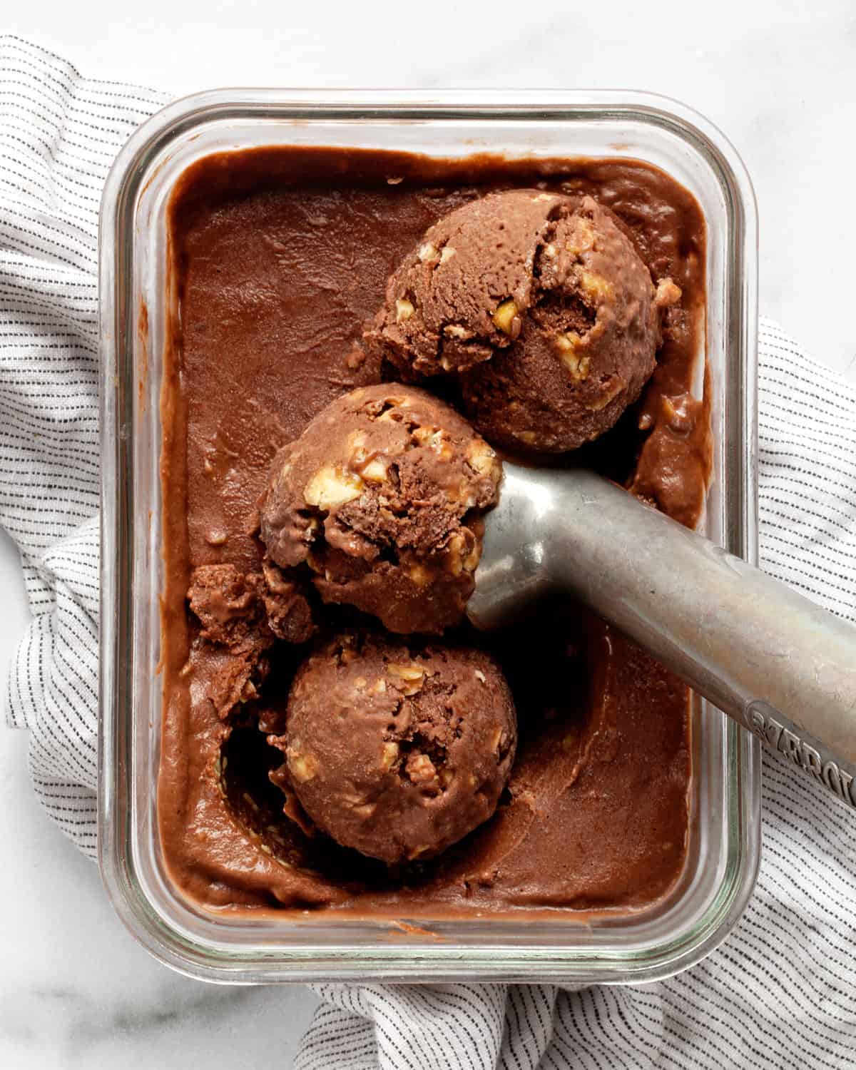 Chocolate nice cream in a container with an ice cream scoop.