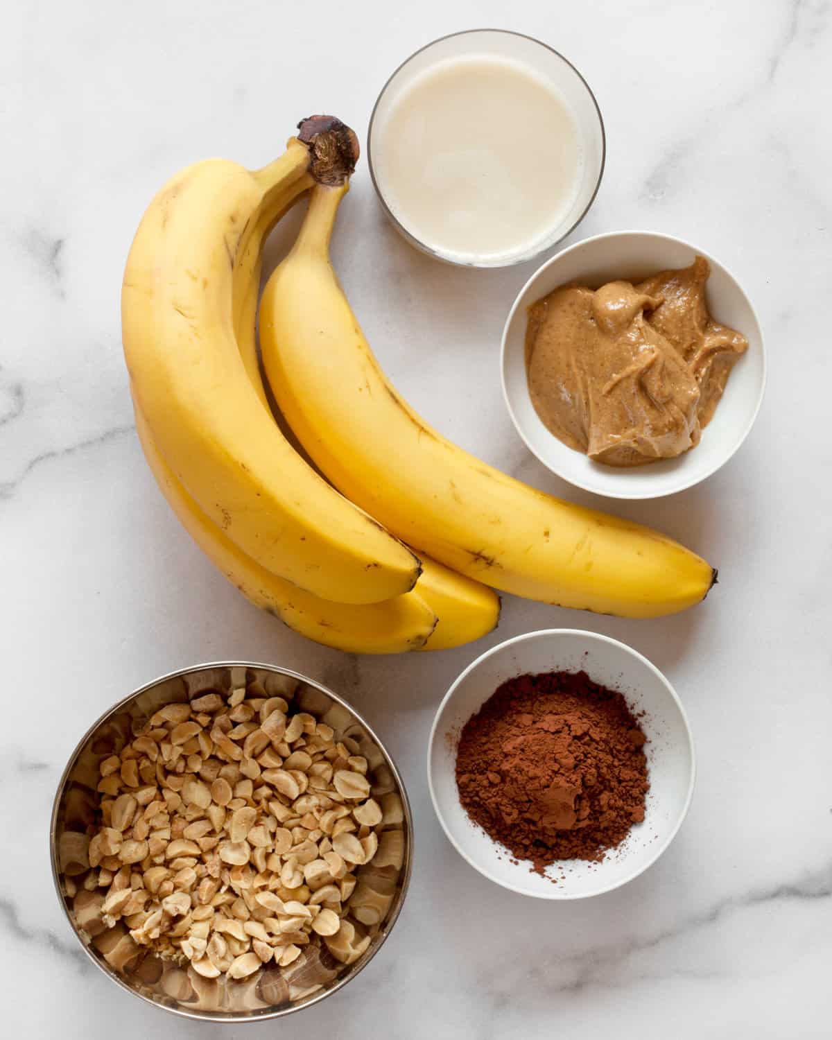 Ingredients including bananas, milk, peanut butter, cocoa powder and chopped peanuts.