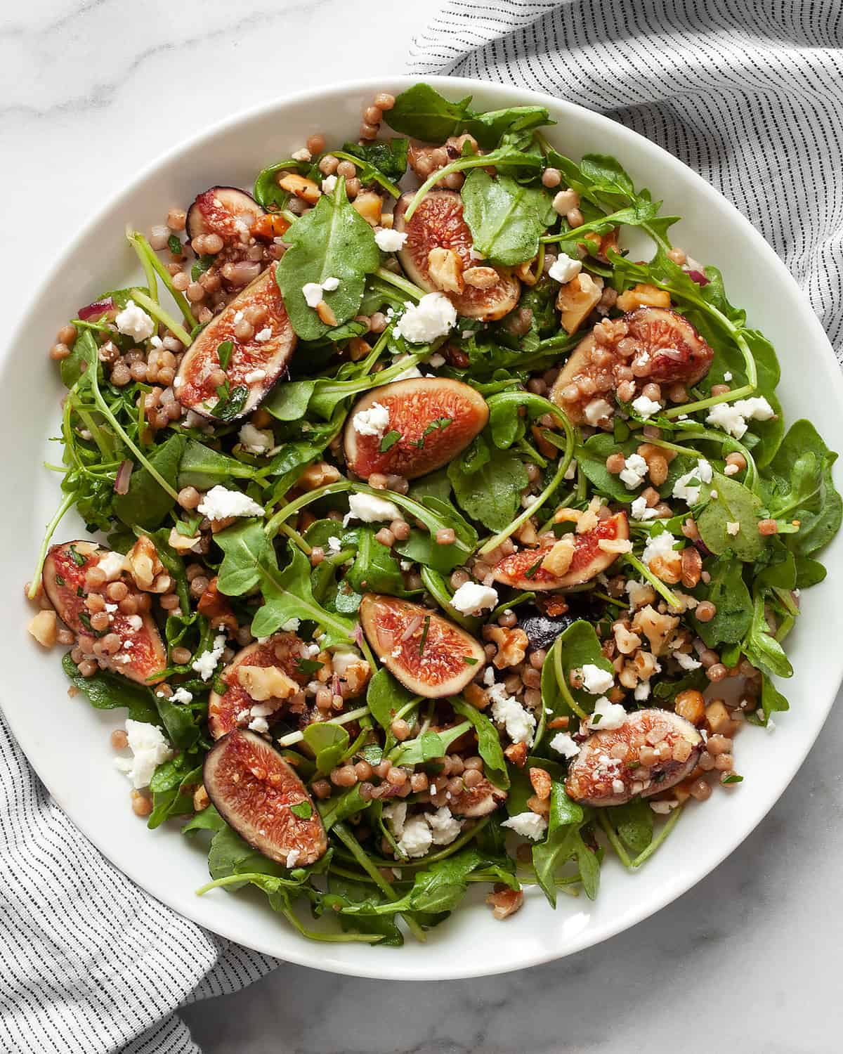 Arugula salad with figs, goat cheese and couscous on plate.