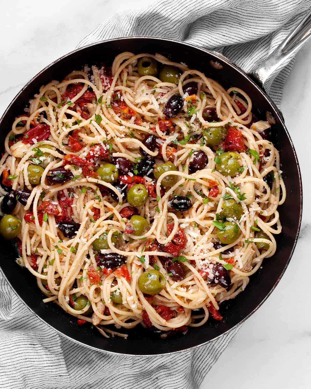 Spaghetti in a skillet with assorted antipasti.