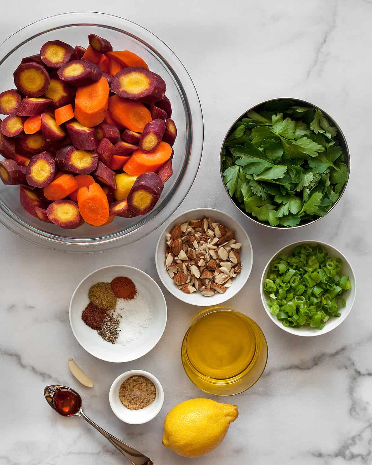 Ingredients including rainbow carrots, scallions, almonds, parsley, cilantro, almonds, spices and olive oil.