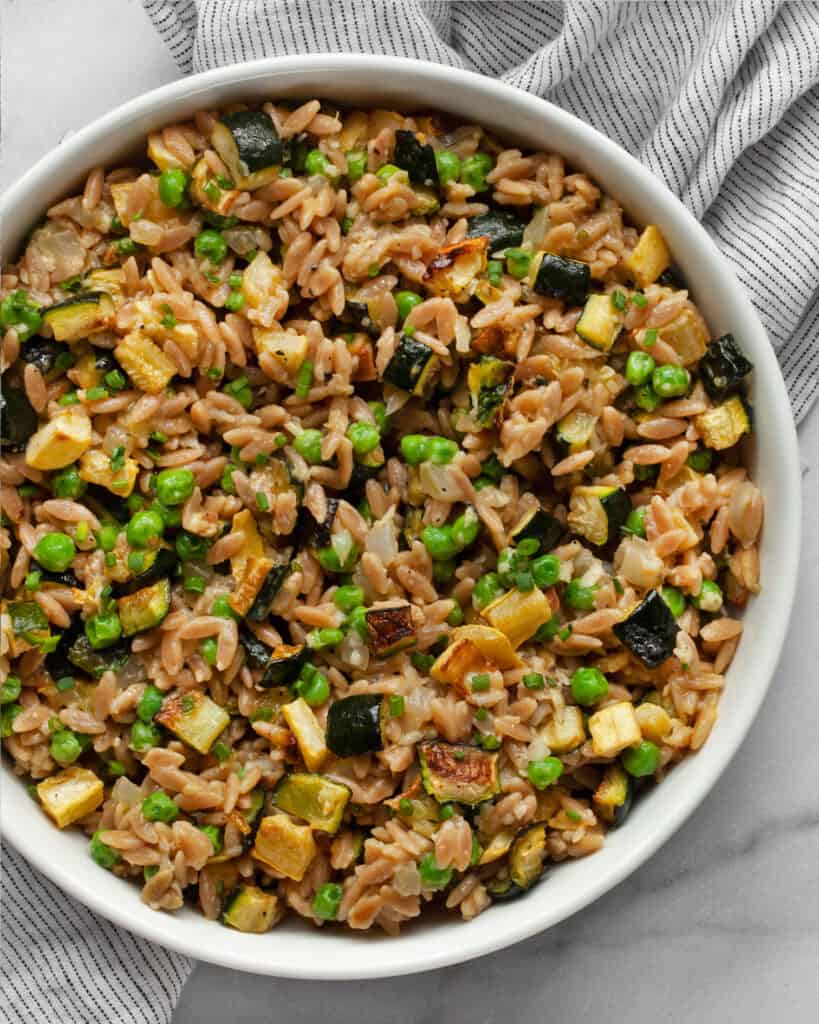 Bowl of orzo with squash, zucchini and peas.