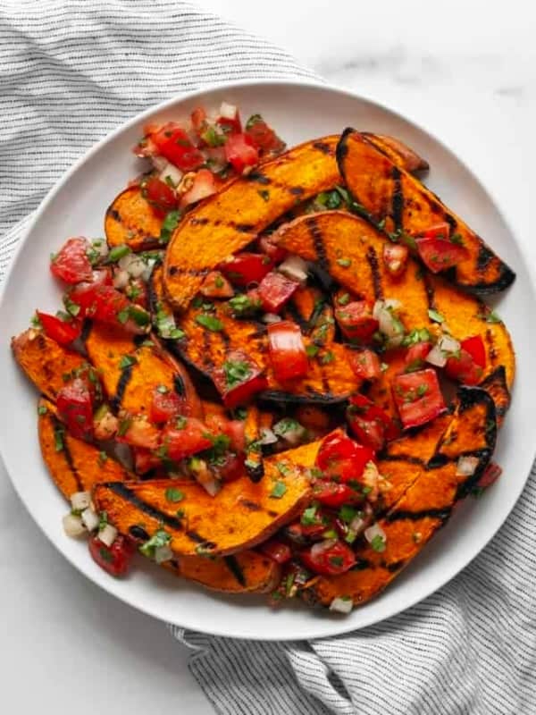 Sweet potatoes topped with pico de gallo on a plate.