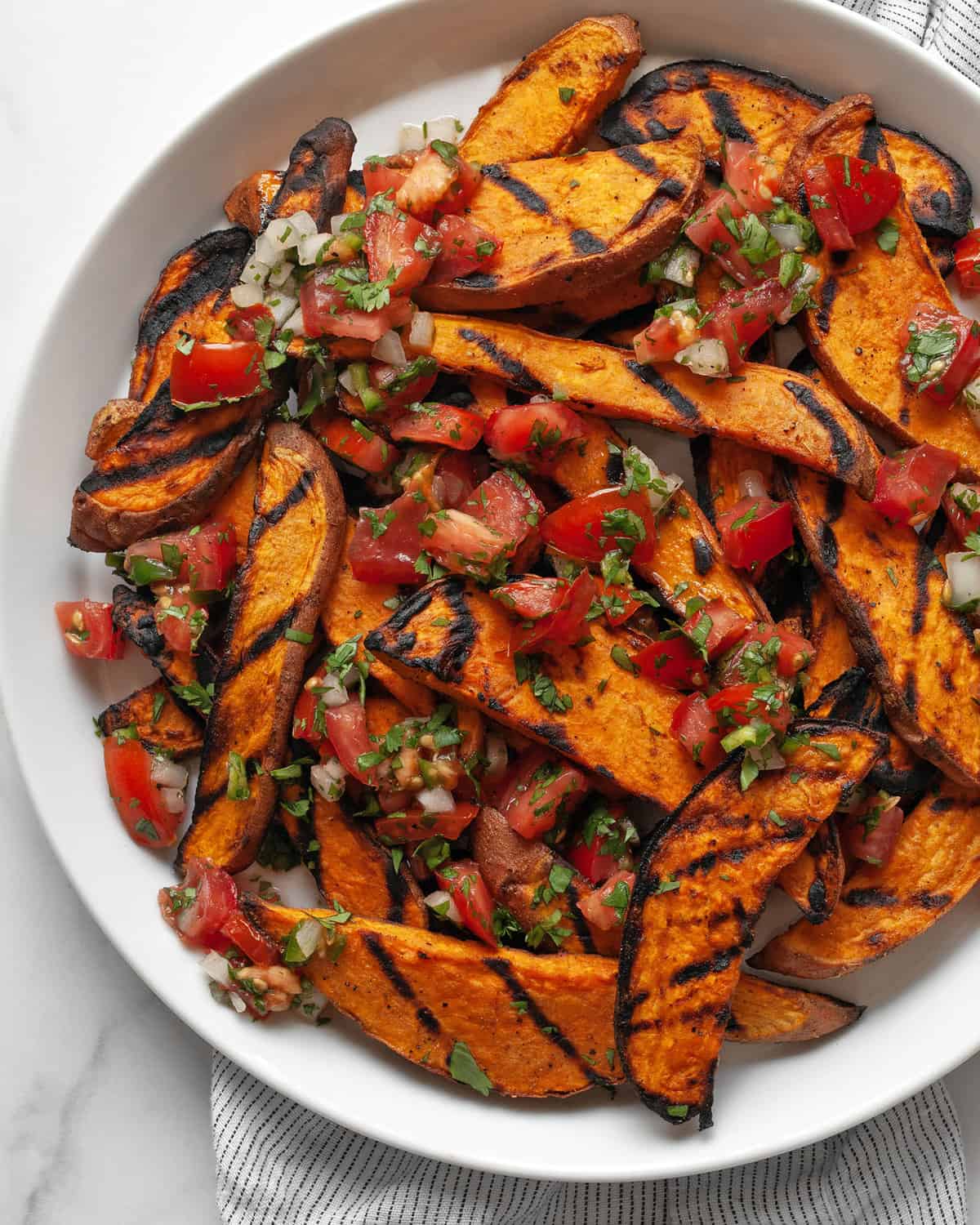 Sweet potatoes topped with pico de gallo on a plate.