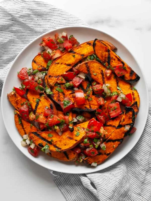 Sweet potatoes topped with pico de gallo on a plate.