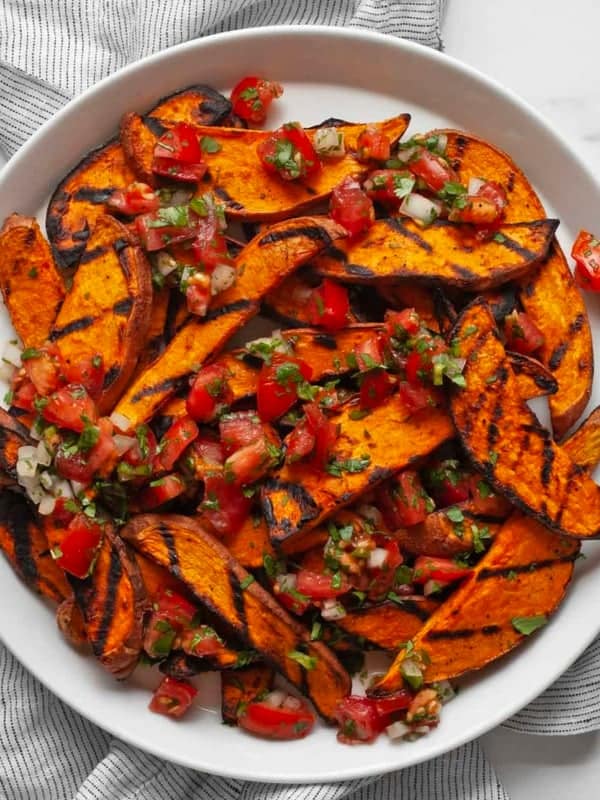 Sweet potatoes topped with pico de gallo on a plate.