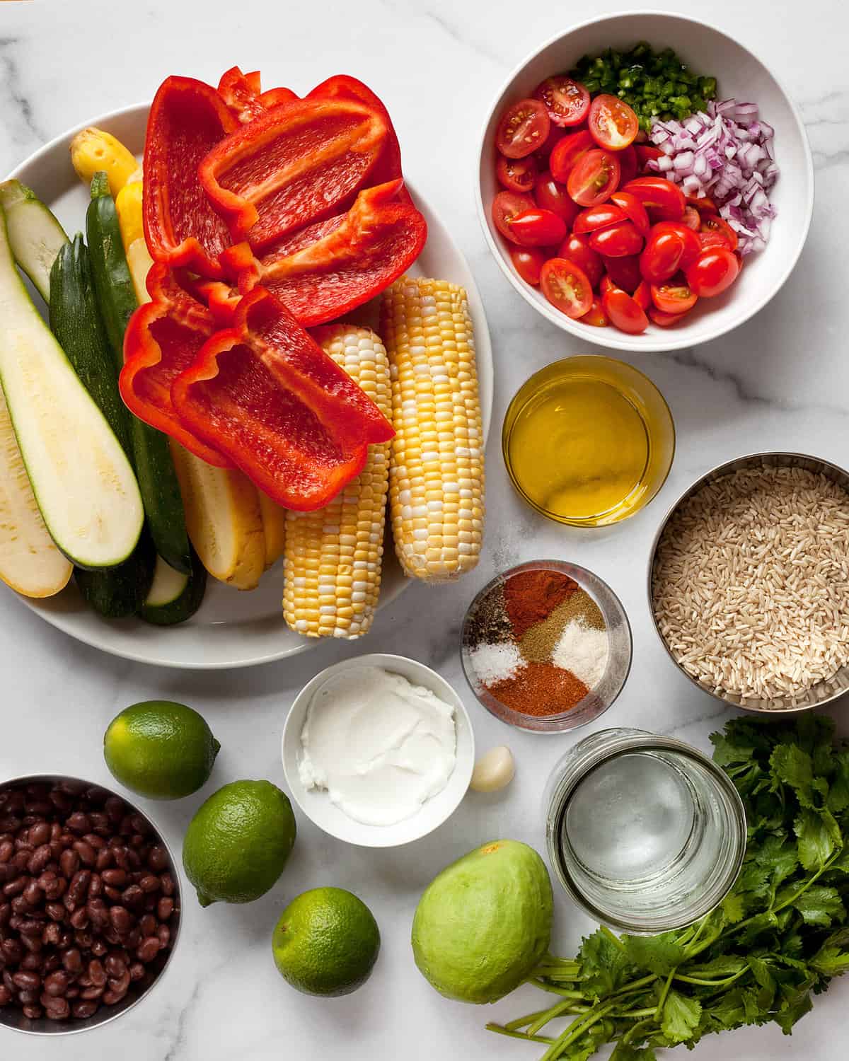 Ingredients including zucchini, squash, peppers, corn, spices, limes, cilantro, rice and more.