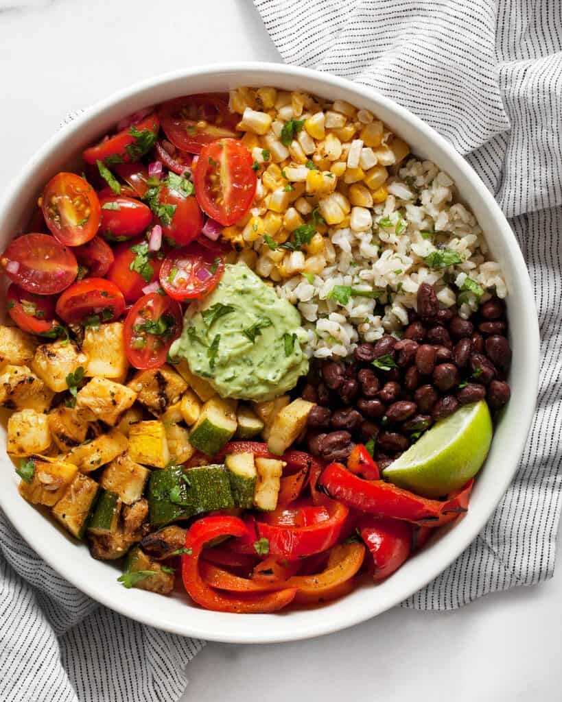 Assembled grilled veggie burrito bowl with squash, zucchini, peppers, black beans and pico de gallo.