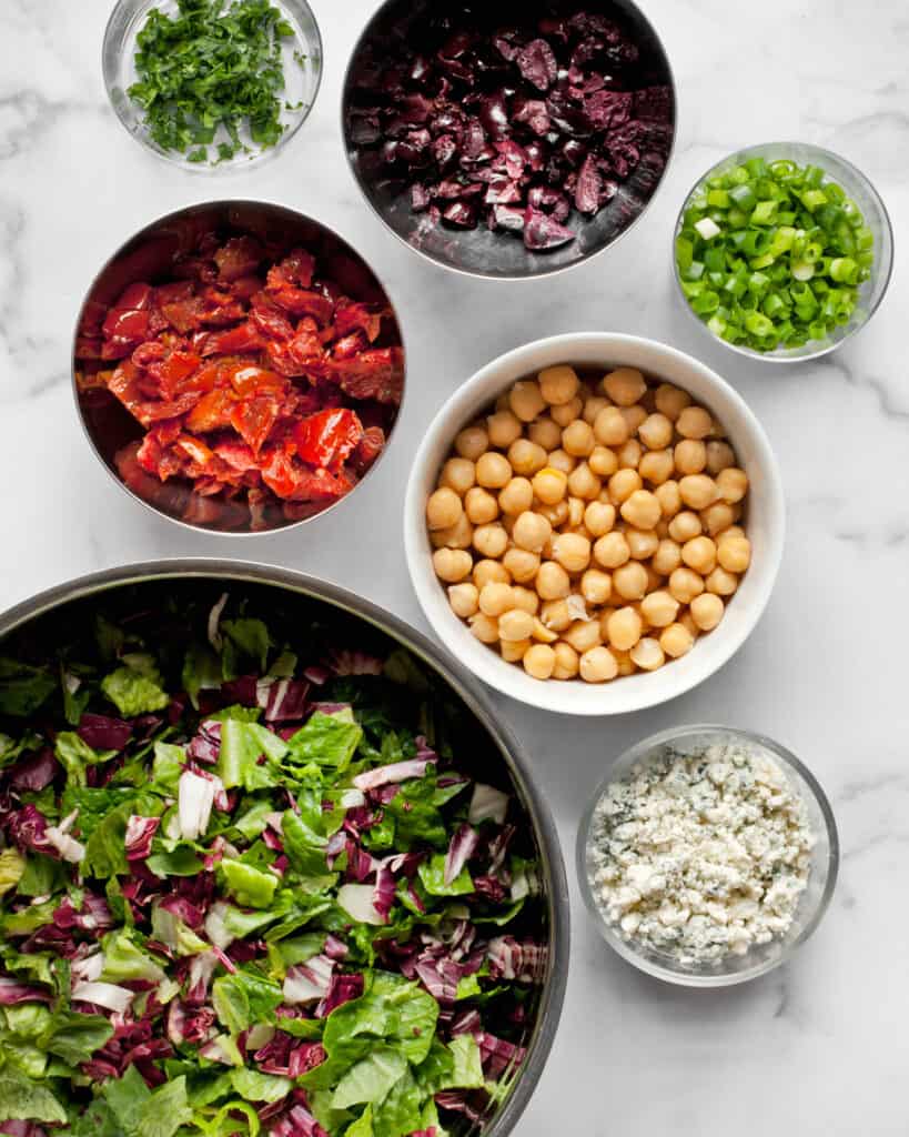Ingredients for classic chopped salad including romaine, radicchio, roasted tomatoes, olives and chickpeas