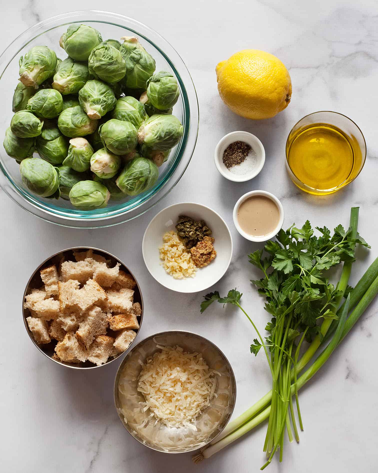 Ingredients for salad including brussels sprouts, parsley, lemon, tahini, scallions, olive oil, Parmesan and bread 