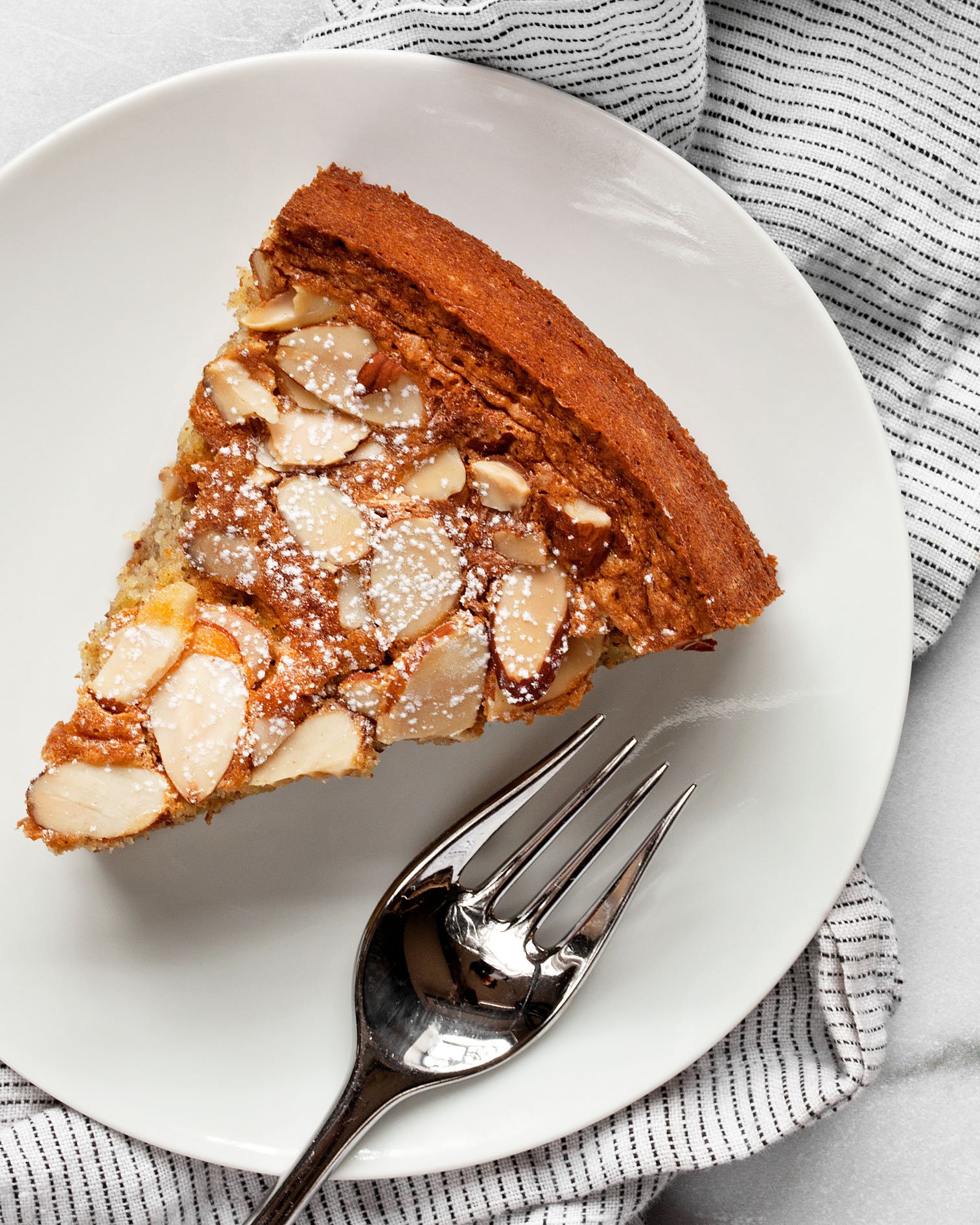 Slice of almond cake with a fork on a plate.