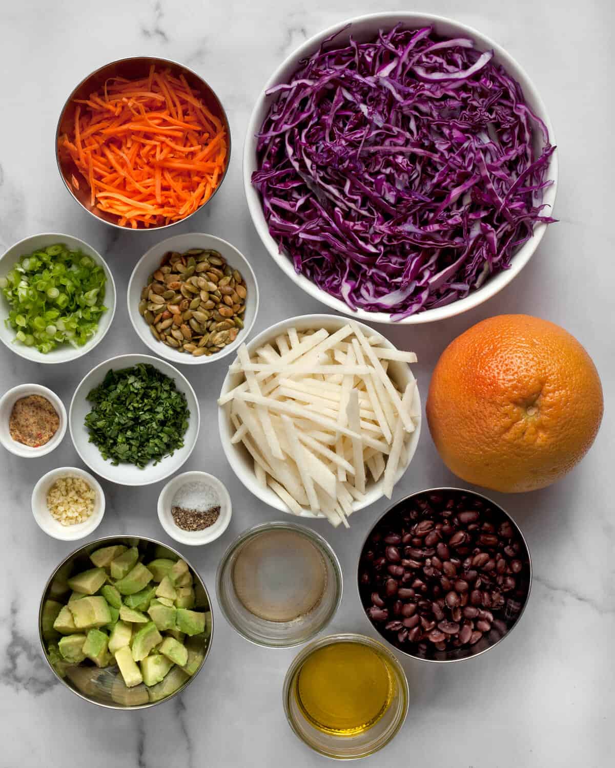 Ingredients for salad including jicama, cabbage, carrots, grapefruit, black beans, avocado, cilantro and pepitas.