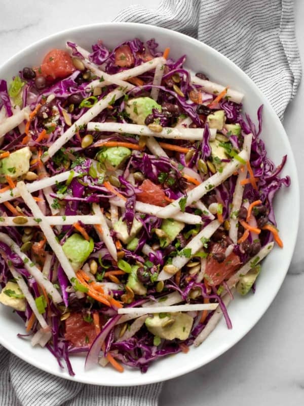 Salad with jicama, red cabbage, carrots, avocado, grapefruit and black beans on plate.