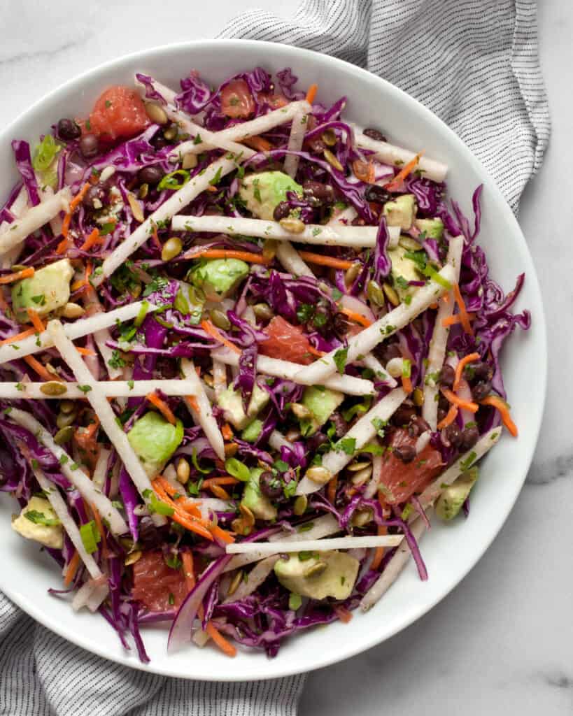 Salad with jicama, red cabbage, carrots, avocado, grapefruit and black beans on plate.