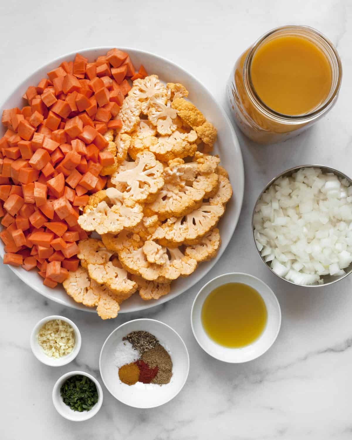 Ingredients including sweet potatoes, cauliflower, vegetable broth, onions, olive oil, seasonings, garlic and parsley.