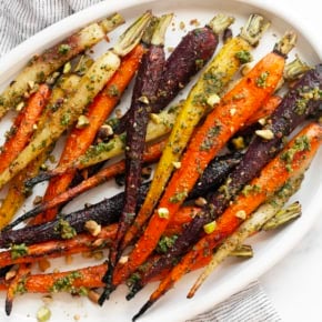 Roasted rainbow carrots with carrot top pesto on a serving plate.