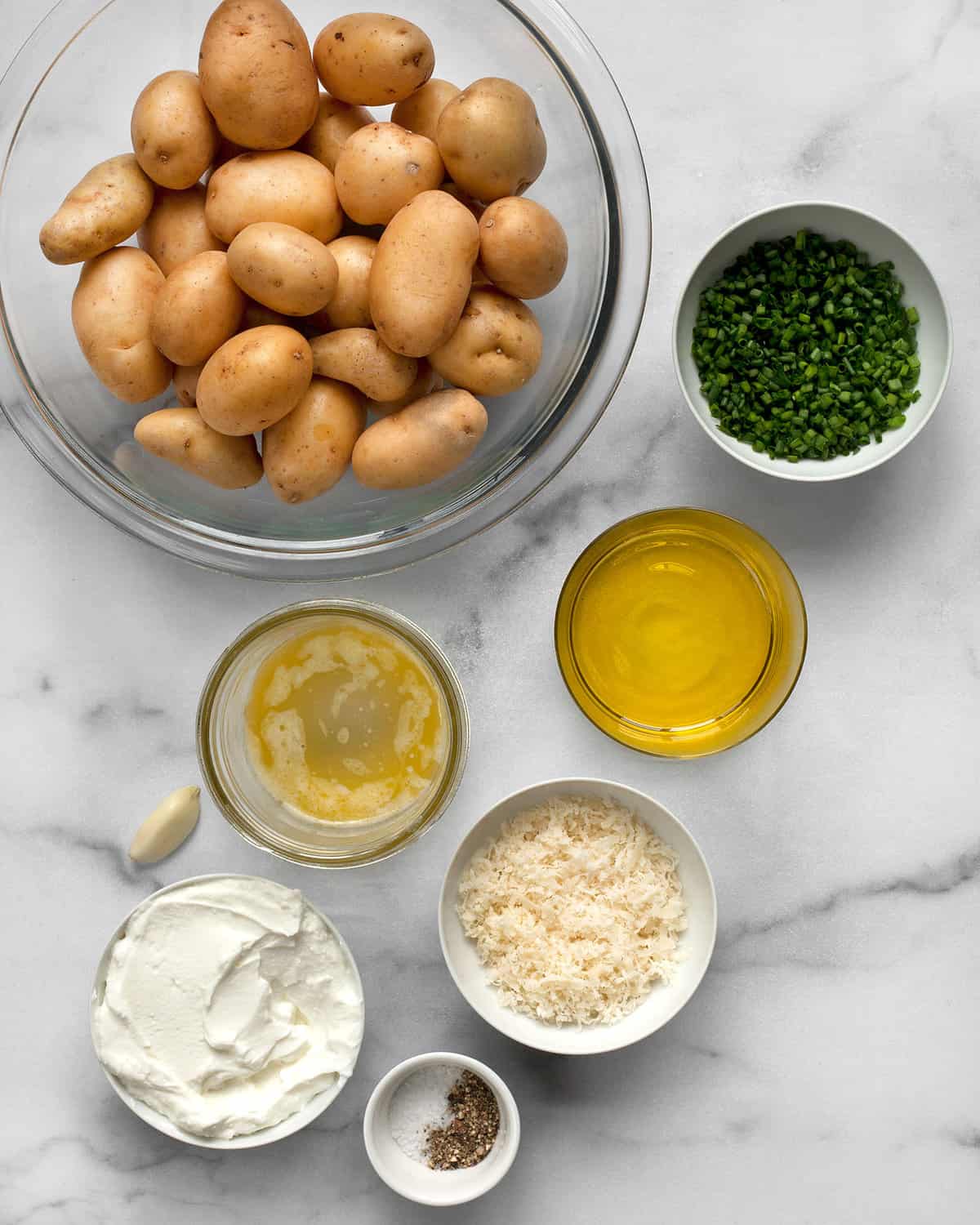 Ingredients including baby potatoes, chives, olive oil, melted butter, Parmesan cheese, salt, pepper and Greek yogurt.