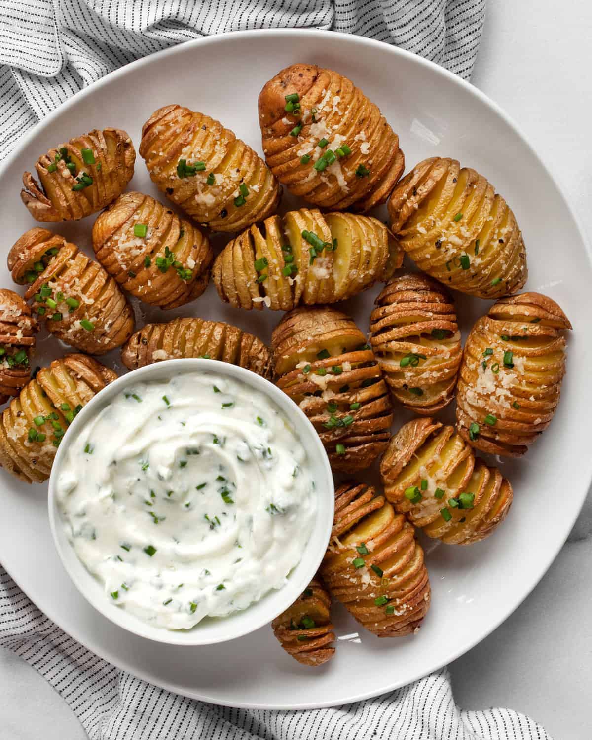 Mini hasselback potatoes on a plate with herby yogurt dip in a small bowl.