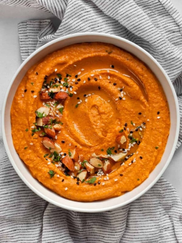 Red pepper hummus garnished with chopped almonds, sesame seeds and parsley.