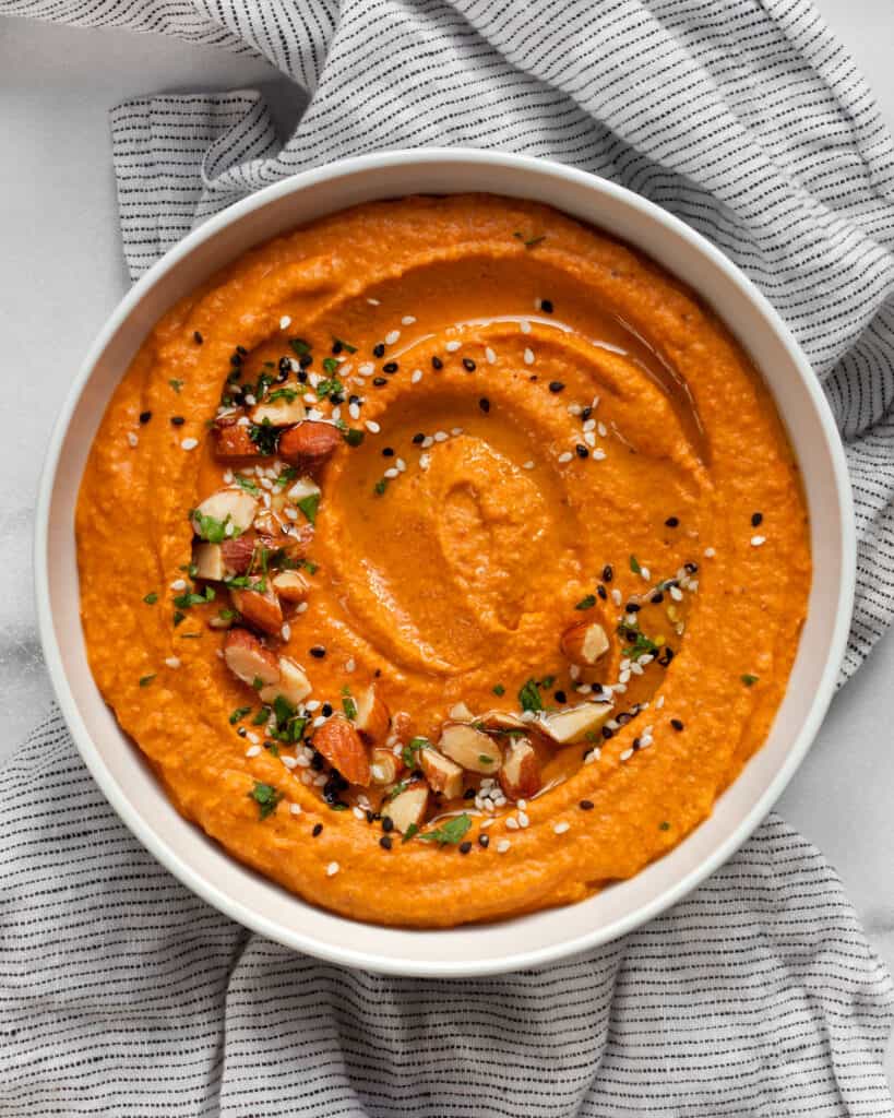 Red pepper hummus garnished with chopped almonds, sesame seeds and parsley.
