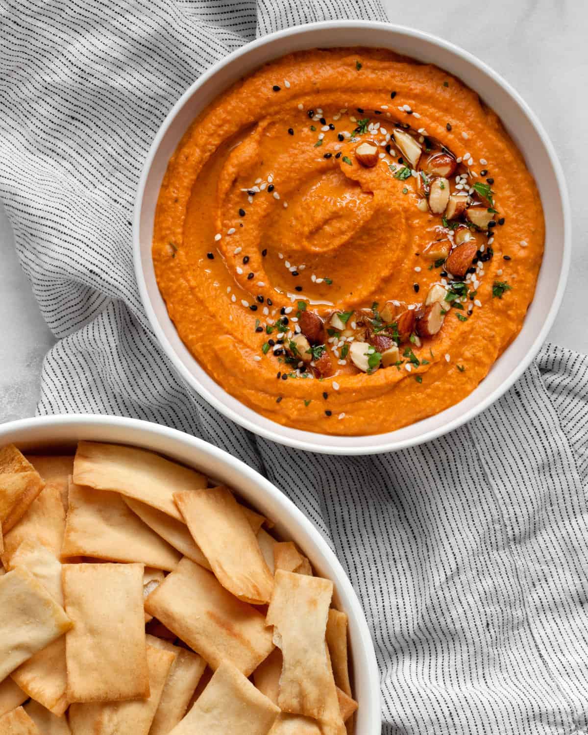 Bowl of red pepepr hummus with a separate bowl of pita chips.