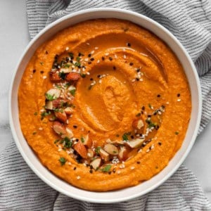 Red pepper hummus garnished with chopped almonds, sesame seeds and parsley.